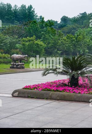 Chongqing, China - May 9, 2010: Statue of hippopotamus in front of green foliage wall with walkway and pink flower bed in front under silver sky. Stock Photo