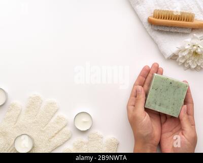 Spa Kit. Hands holding green natural Soap Bar, wooden brush limestone heel stone, candles, towel, flower on light white background with copy space. Hy Stock Photo