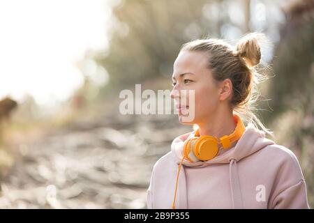 Portrait of beautiful sports woman with hoodie and headphones during outdoors training session.