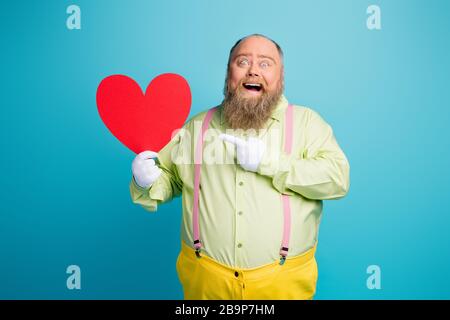 Portrait of his he nice funny funky cheerful cheery crazy man holding in hand demonstrating big large heart card isolated over bright vivid shine Stock Photo