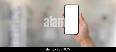 Cropped shot of a man showing blank screen smartphone in blurred glass partition office room background Stock Photo
