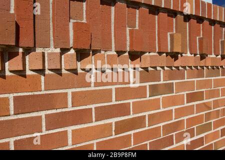 Protruding bricks in geometric shapes decorate the top of this traditional reddish brown brick wall texture background, with sunlight cast shadows Stock Photo