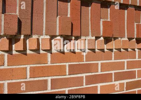 Protruding bricks in geometric shapes decorate the top of this traditional reddish brown brick wall texture background, with sunlight cast shadows Stock Photo