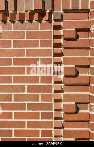 Protruding bricks in geometric shapes decorate the top of this traditional reddish brown brick wall texture background, with sunlight cast shadows Stock Photo