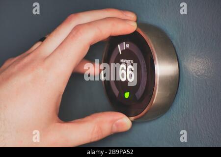 Hand operating smart thermostat to save money. Hand making adjustments by turning knob. Smart home. Stock Photo