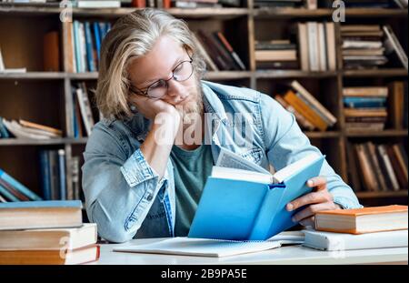 Sleepy tired student in library at desk study for exam. Stock Photo