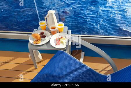 A continental breakfast including bread, rolls, fresh fruit and juice presented on a balcony onboard a cruise ship alongside a writing journal diary. Stock Photo