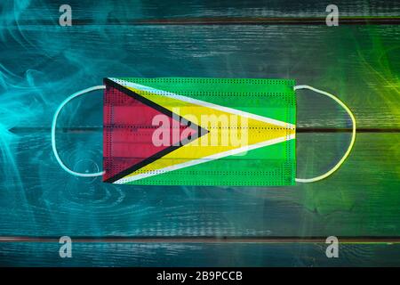 Medical mask for protection against airborne diseases, painted in the national flag of Guyana  on a black background in blue-green smoke. Medical prot Stock Photo