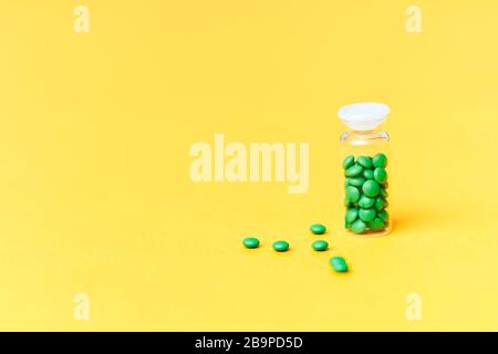 Medical green pills in a glass bottle on yellow background copyspace, health Stock Photo