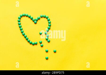 green round pills tablets brocken heart shape on yuellow background Stock Photo