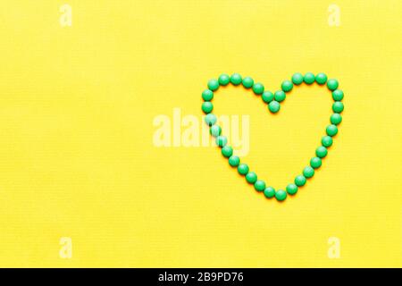 green round pills tablets heart shape on yuellow background Stock Photo