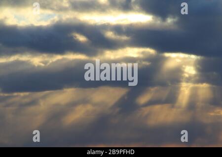 The sun at sunset or dawn behind the clouds, shines through. The sun's rays in the sky. Stock Photo