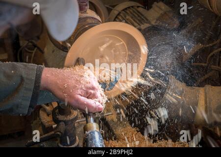 Making a wooden bowl on a lathe in an old small workshop with flying wooden shavings Stock Photo