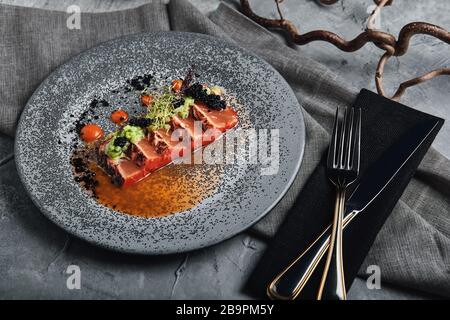 Salmon steak sliced in beautiful slices drenched in a sauce with vegetables. Traditional Italian cuisine. copy space, gray background. Stock Photo