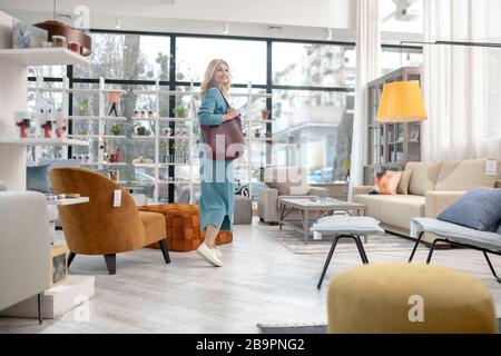 Woman with a burgundy bag walking through the furniture salon. Stock Photo