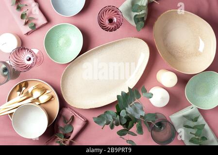 Table served for festive spring dinner. Top view. Copy space. Empty serving plates, bowls, candles and eucalyptus flowers on pink shabby background Stock Photo
