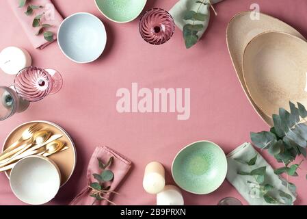 Table served for festive spring dinner. Top view. Copy space. Empty serving plates, bowls, candles and eucalyptus flowers on pink shabby background Stock Photo