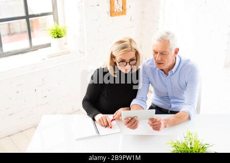 High angle shot of senior couple calculating their finances together at home while sitting at desk and using digital tablet. Stock Photo