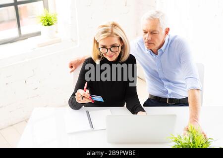 High angle shot of happy senior couple shopping online. Attractive elderly woman holding bank card in her hand while senior man sitting behind their l Stock Photo