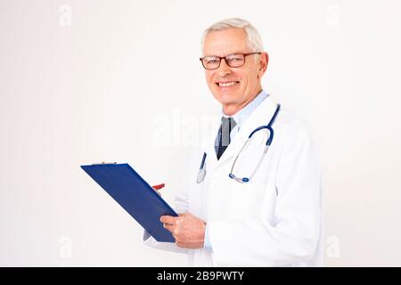Portrait shot of senior male doctor with stethoscope around his neck holding in hands a clipboard while standing at isolated white background. Stock Photo