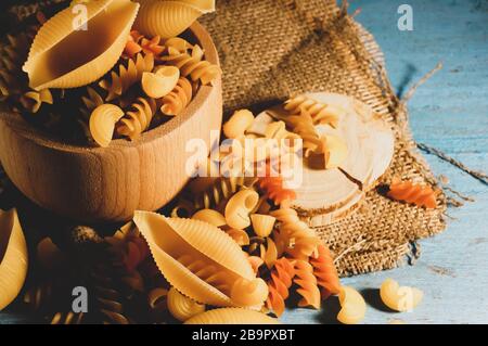 Various kinds of pasta on a wooden background of blue color. Farfalle, fettuccine, noodles, fusilli and penne. Stock Photo