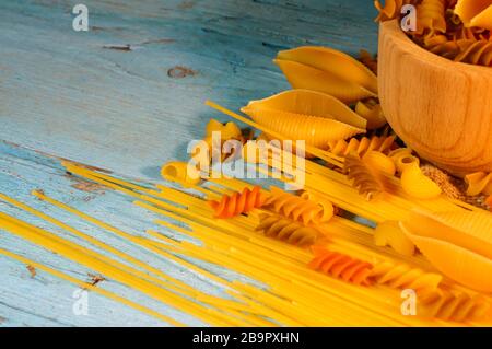 Various kinds of pasta on a wooden background of blue color. Farfalle, fettuccine, noodles, fusilli and penne. Stock Photo