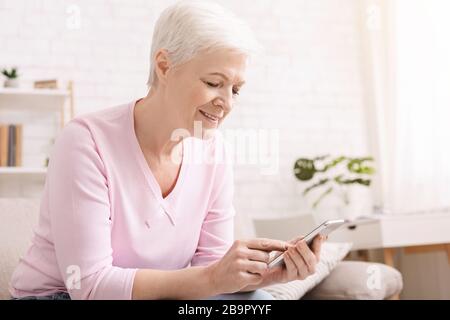 Senior woman chatting on smartphone with family at home Stock Photo