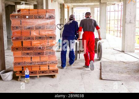 Construction workers are using their manpower to manage wheelbarrow with fresh mortar at construction site. Stock Photo