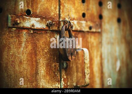 The old rusty abandoned gate is tightly closed on an old large barn lock with a small keyhole. Stock Photo