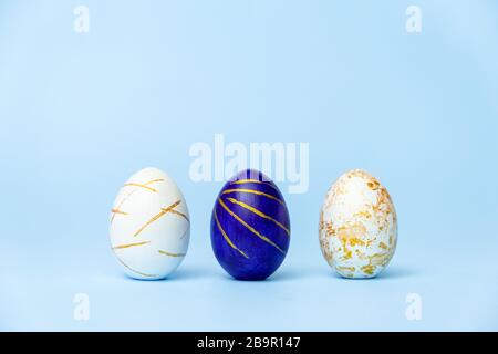Three easter trendy colored classic blue and golden decorated eggs on blue background. Happy Easter card with copy space for text Minimal easter style Stock Photo