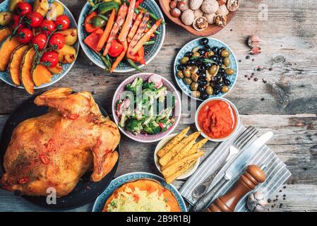 Thanksgiving dinner cooking preparation. Traditional dishes: chicken, pumpkin, corn, vegetables salads over wooden background. Top view, copy space. A Stock Photo