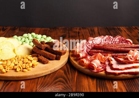 Assorted beer snacks on a wooden table with copy space. Sausage, ham, bacon. Salty snack chips, croutons, peanuts, wasabi nuts. Stock Photo