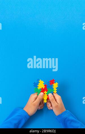 World autism awareness day concept. Child hands holding colorful puzzle heart on blue background Stock Photo