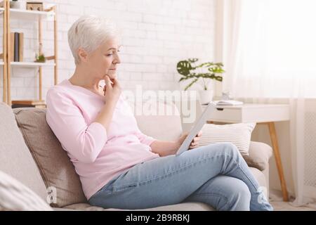 Worried senior woman reading Covid-19 news articles Stock Photo