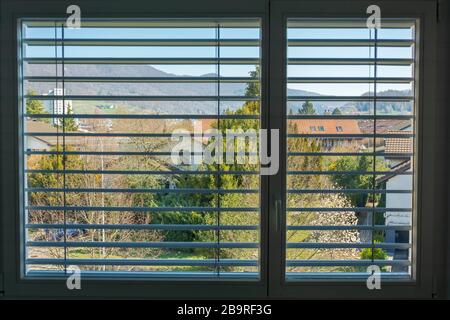 Corona Covid-19 quarantine window view from home during lock down. View on village through half closed roller shutter. Stock Photo