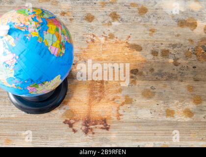 Pandemic concept, wooden board with many spots reminiscent of the spread of the coronavirus, on the left is visible a blurry globe. Stock Photo