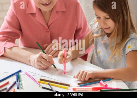Mature woman with her lovely granddaughter drawing Christmas tree together in kitchen Stock Photo