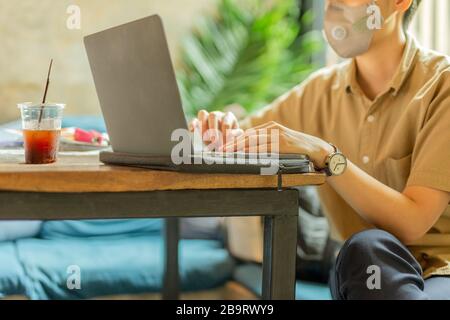 Woman in protective mask working on laptop in cafe.
