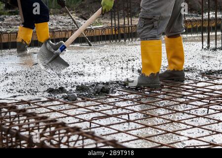 two bricklayers at work on a construction site during the laying of concrete to build the foundations of a house Stock Photo