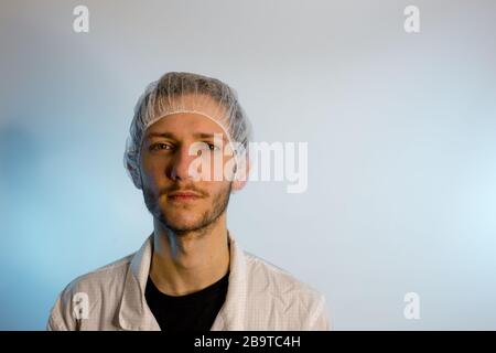 An adult male dressed in a white lab coat with a hair net on. Ready to work in a clean room or laboratory Stock Photo
