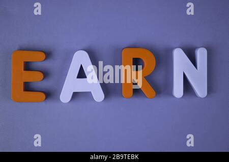 Earn word written with different colored letter blocks arranged on a light blue background Stock Photo