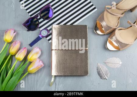A gold notebook with women's shoes, tulips, glasses and a watch on a concrete background. Flet lay Stock Photo