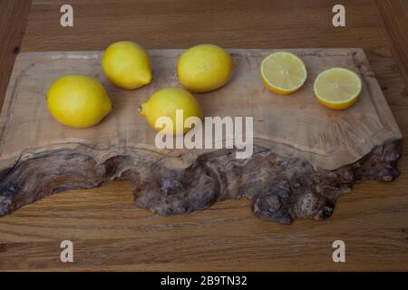 Lemons on a wooden chopping board, whole and in two halves Stock Photo