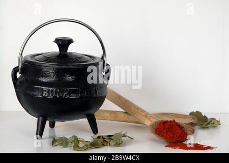 Three-legged cast iron black pot, wooden spoons and paprika on white shelf Stock Photo