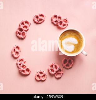 Cup of coffee with art heart shape and Strawberry flavoured yogurt covered pretzels on pink background. Love concept. Flat lay, top view Stock Photo
