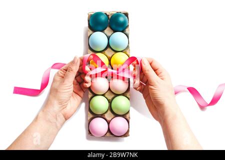 Easter eggs decoration on white background.  Woman's hands decorating with ribbon a box of colorful eggs Stock Photo