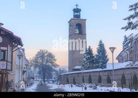 Bansko, Bulgaria - December 6, 2019: Pirin street in old town, bell tower and wall of Sveta Troitsa Church Stock Photo