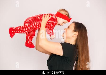 Mom holds a newborn daughter in her arms. Laughter and joy. Red clothes. The concept of family, motherhood and child care. Stock Photo