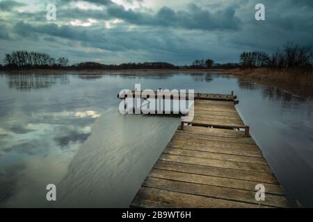 Wooden jetty on a lake and dark clouds on sky, evening view Stock Photo