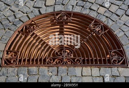 Paving stones background with rusty metal manhole, iron manhole cover for the drainage of the walkway Stock Photo